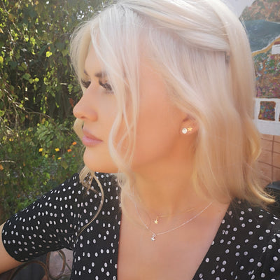 model with blonde hair wearing black dress, layered star necklaces and sun moon star earrings, garden background