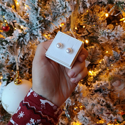 A handheld lulu&levi box displaying a pair of soft white large pearl earrings, in front of a christmas tree 