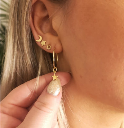A hand showing off the ear of a woman wearing gold endless hoops and the sun moon star gold earring studs 
